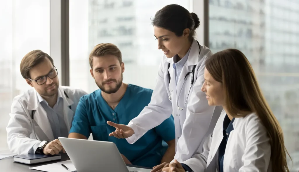 Four healthcare professionals discussing a case around a laptop