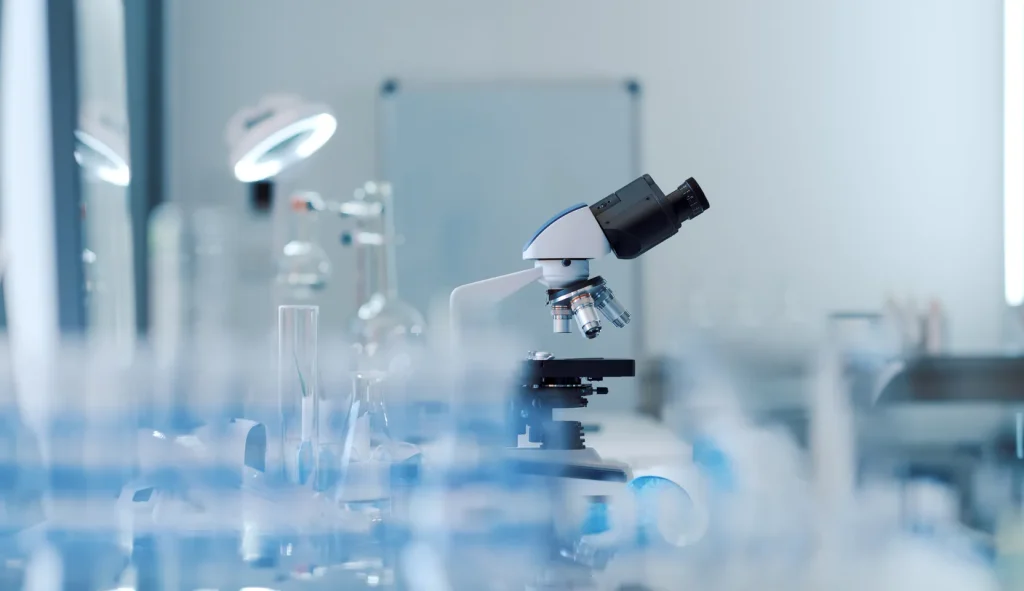 Laboratory microscope surrounded by glass vials on a bench