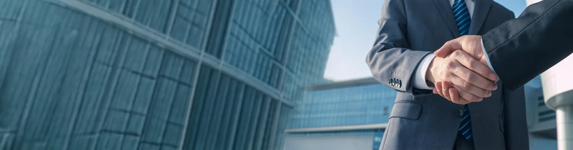 Two people in suits shaking hands in front of an office building