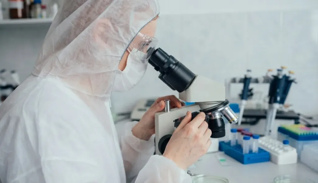 Scientist in protective clothing looking into a microscope