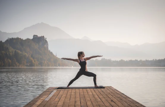 A person practising yoga on a wooden pier by a mountain lake